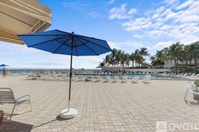 Hollywood condo for rent - A blue umbrella stands on a patio overlooking a pool and beach.