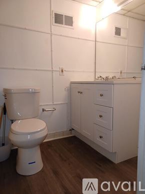 Knoxville condo for rent - A white toilet in a small bathroom with wooden floors and white walls.