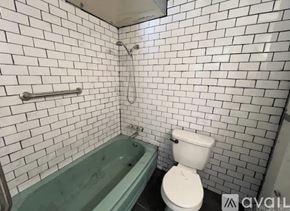 North Little Rock house for rent - A white toilet is next to a green bathtub in a bathroom with white tiled walls.