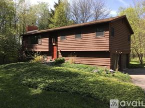 Ithaca house for rent - A brown house with a red door is surrounded by greenery.
