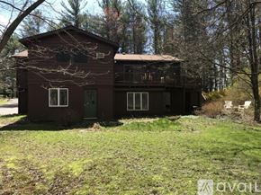 Ithaca house for rent - A brown house with a balcony and a green door is surrounded by trees.