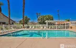 Palm Desert condo for rent - A pool surrounded by palm trees and deck chairs.