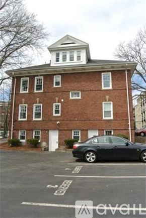 Boston apartment for rent - A black car is parked in a parking lot in front of a brick building.