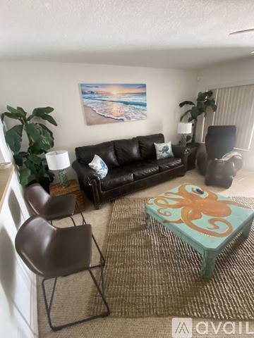 Lecanto townhouse for rent - A living room with a black couch, a brown chair, a green ottoman, and a painting on the wall.