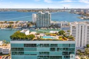 North Bay Village apartment for rent - A modern glass building with a pool on the roof is surrounded by other buildings and a body of water.
