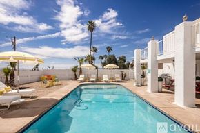 Lake Havasu City house for rent - A pool with a white umbrella and chairs in front of a white building.