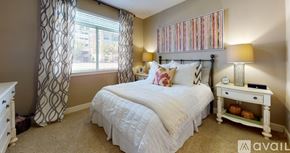 Irving apartment for rent - A bedroom with a white bed, a white nightstand, and a window with curtains.