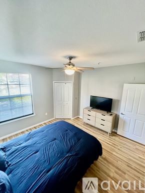 Sarasota condo for rent - A bedroom with a bed covered in a blue sheet, a ceiling fan, and a television on a cabinet.