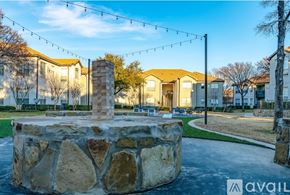 Fort Worth apartment for rent - A stone fountain is in the middle of a grassy area with houses in the background.