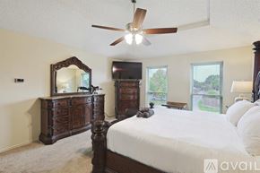 Lewisville house for rent - A bedroom with a large bed, a dresser with a mirror, and a ceiling fan.
