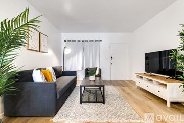 Virginia Gardens apartment for rent - A living room with a grey couch, a black coffee table, and a television on a wooden stand.