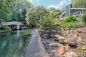 Clayton house for rent - A house is situated by a body of water with a concrete walkway leading to it.