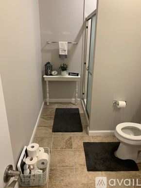 Cincinnati apartment for rent - A bathroom with a toilet, a small table with a plant, and a basket of toilet paper.