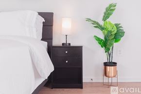 Tysons apartment for rent - A bedroom with a bed, a nightstand with a lamp, and a plant.