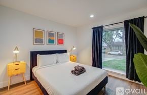 Houston house for rent - A bedroom with a large bed, a nightstand with a lamp, and a window with a view of a car and trees outside.