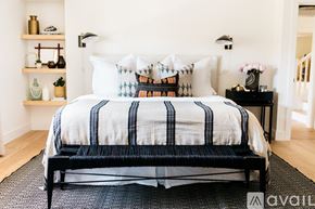 Laguna Beach house for rent - A bed with a white and blue striped comforter and pillows is in the foreground of a room with a black chair and a small table with a vase of flowers.
