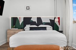 Dallas apartment for rent - A bedroom with a white bed and a wall hanging with black and red shapes.