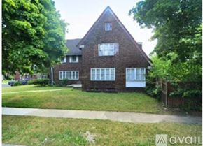 Detroit house for rent - A house with a brown brick exterior and white trim is surrounded by greenery.