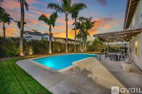Huntington Beach house for rent - A pool surrounded by palm trees and a house with a patio.