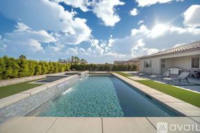 La Quinta house for rent - A large swimming pool with a stone wall and a house in the background.