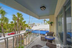 St. Pete Beach apartment for rent - A balcony with a table and chairs overlooking a pool and trees.
