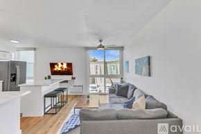 San Diego condo for rent - A modern living room with a grey sofa and a kitchen area with a fridge and bar stools.