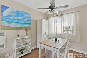 San Diego condo for rent - A dining room with a white table and chairs, a ceiling fan, and a beach scene on the wall.