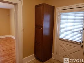 Brownsville apartment for rent - A tall brown wooden wardrobe stands in a room with a white door and window with blinds.