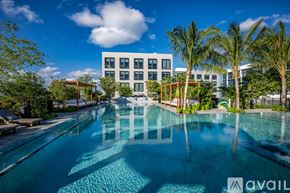 Miami apartment for rent - A large swimming pool in front of a modern building with palm trees.