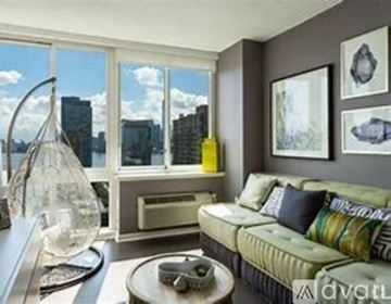 Jersey City apartment for rent - A living room with a green couch and a large window overlooking a city.