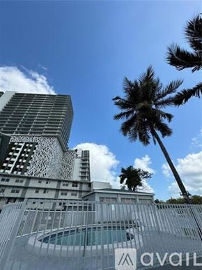 Miami apartment for rent - A tall building with a unique design stands next to a palm tree.