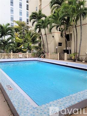 Miami apartment for rent - A swimming pool surrounded by palm trees and a building in the background.