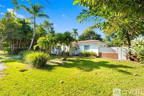 Key Biscayne house for rent - A house with a white fence and a green lawn is surrounded by trees.