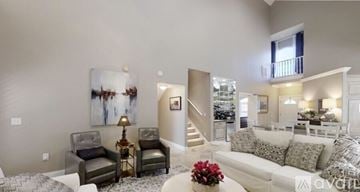 Gulf Shores apartment for rent - A living room with a grey couch, a grey and white rug, a grey and black chair, a table with a vase of red flowers, a painting on the wall, and a staircase leading to the upper floor.