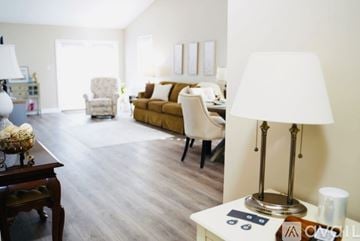 Crown Point apartment for rent - A living room with a brown couch, a white chair, and a table with a lamp and a vase of flowers.