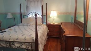 Norwood apartment for rent - A bed with a white comforter and a wooden nightstand with a lamp on it.