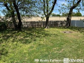 Tulsa apartment for rent - A grassy area with trees and a fence in the background.