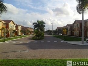 Hialeah townhouse for rent - A street view of a residential area with houses on both sides and a pedestrian crossing in the middle.