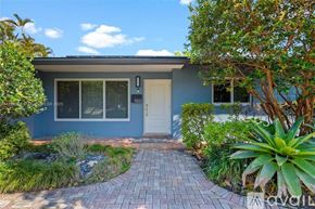 Miami house for rent - A house with a blue exterior and a white door is surrounded by greenery.