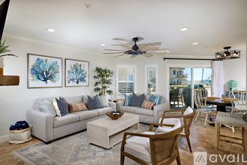 Oceanside apartment for rent - A living room with a grey couch, a wooden chair and a ceiling fan.