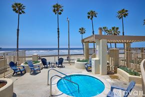 Oceanside apartment for rent - A pool area with a hot tub, chairs, and palm trees.