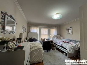 Boston apartment for rent - A bedroom with two beds, one with a white comforter and the other with a black comforter, a dresser with a mirror, and a window with curtains.