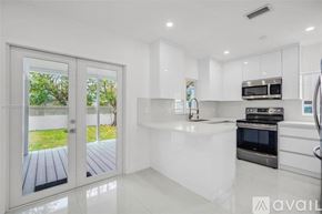 Miami house for rent - A modern kitchen with white cabinets and appliances, a large island, and a view of a deck through the sliding glass doors.