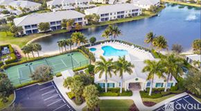 Fort Myers house for rent - A tennis court is surrounded by palm trees and a pool.