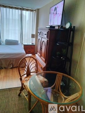 Honolulu condo for rent - A bedroom with a bed, a chair, a glass table and a television.