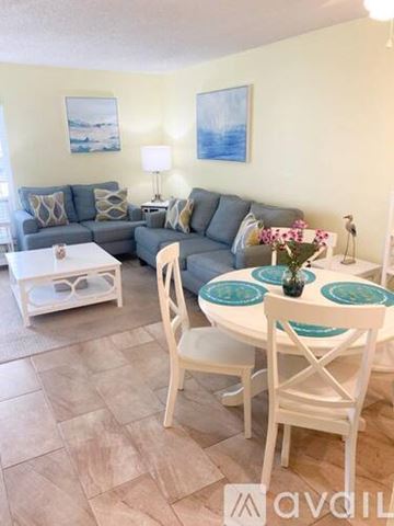 Madeira Beach condo for rent - A living room with a grey couch, a white coffee table, and a white dining table with chairs.