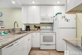 Madeira Beach condo for rent - A kitchen with white cabinets and appliances, a sink, and a refrigerator.