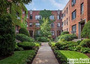 Brookline apartment for rent - A pathway leads through a green and leafy courtyard between two red brick buildings.
