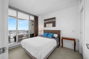 Calgary apartment for rent - A bedroom with a large bed and a view of the city.