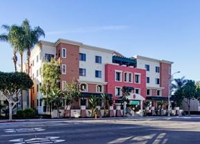 Fullerton apartment for rent - A multi-story building with a red and beige facade is surrounded by palm trees.